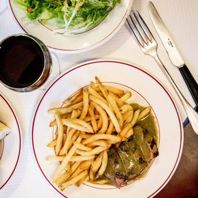 plat de viande avec sa sauce et ses frites et un verre de vin rouge